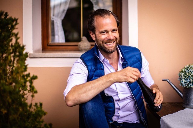 der Winzer des Weingut Tegernseerhof an einem Tisch und lächelt freundlich