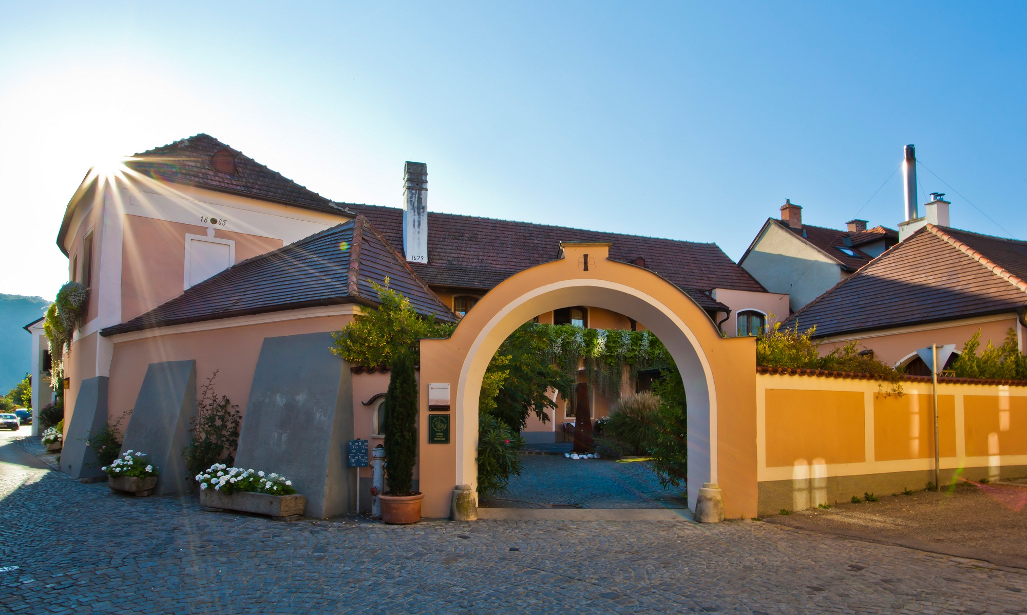 das Gebäude des Weingut Tegernseerhof mit einem imposanten Torbogen als Eingang - gelb/weiß im klassischen Stil