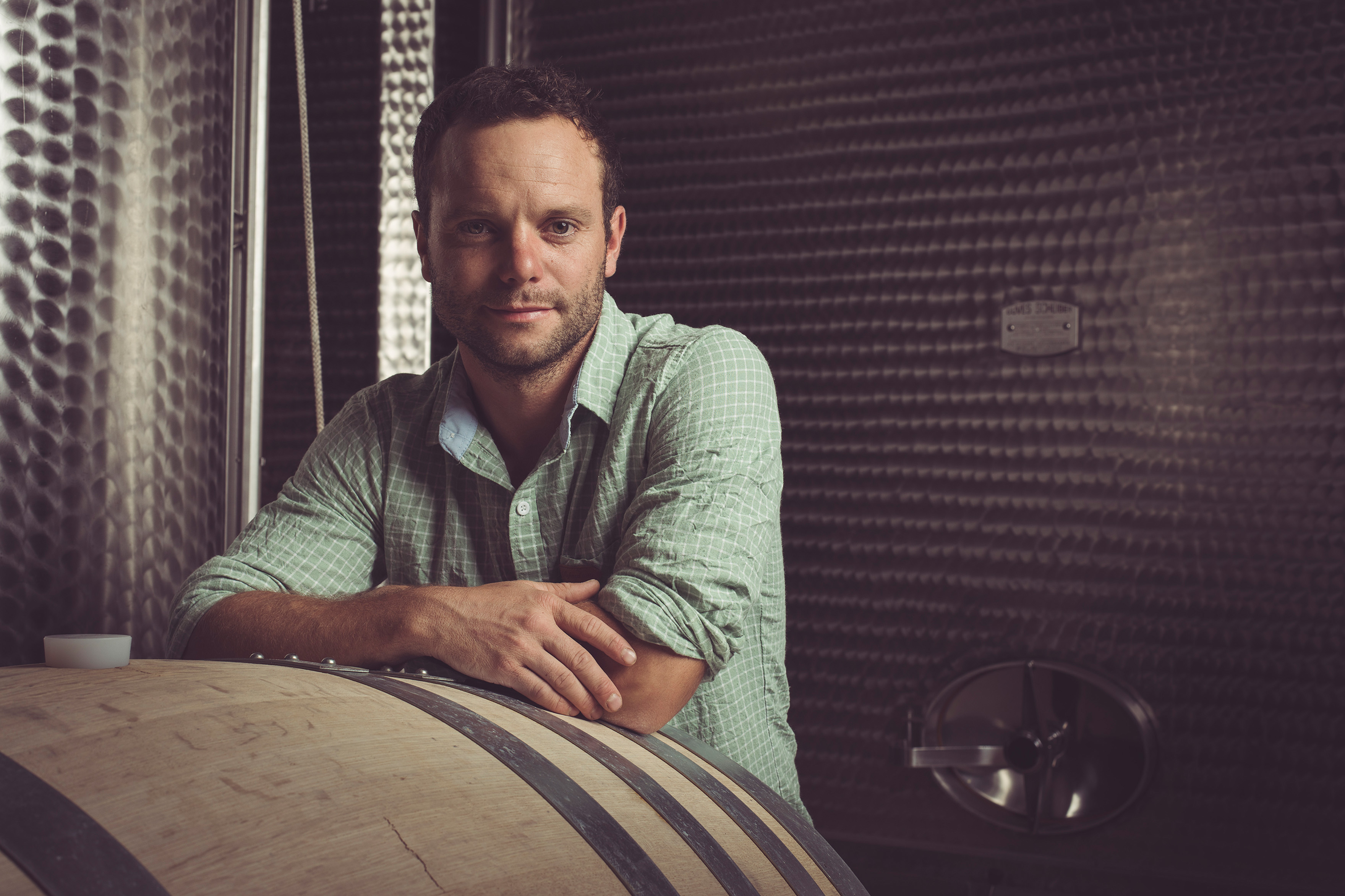 Winzer mit grünem Hemd und aufgekrämpelten Ärmeln lehnt an einem Weinfass